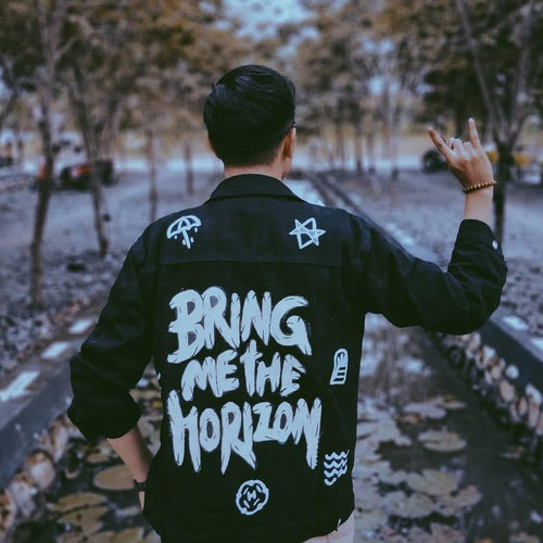 Person wearing a black jacket with 'Bring Me the Horizon' text and graphics, standing on a path with trees.