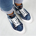 navy blue denim sneakers with white soles worn with jeans on a light gray background