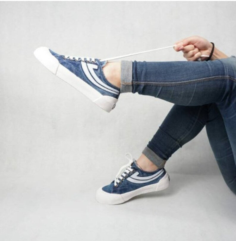 Person wearing Ultimate Denim Tie Sneakers with white soles on a light gray background
