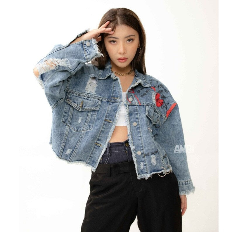 Woman wearing a distressed denim jacket with patches on a white background