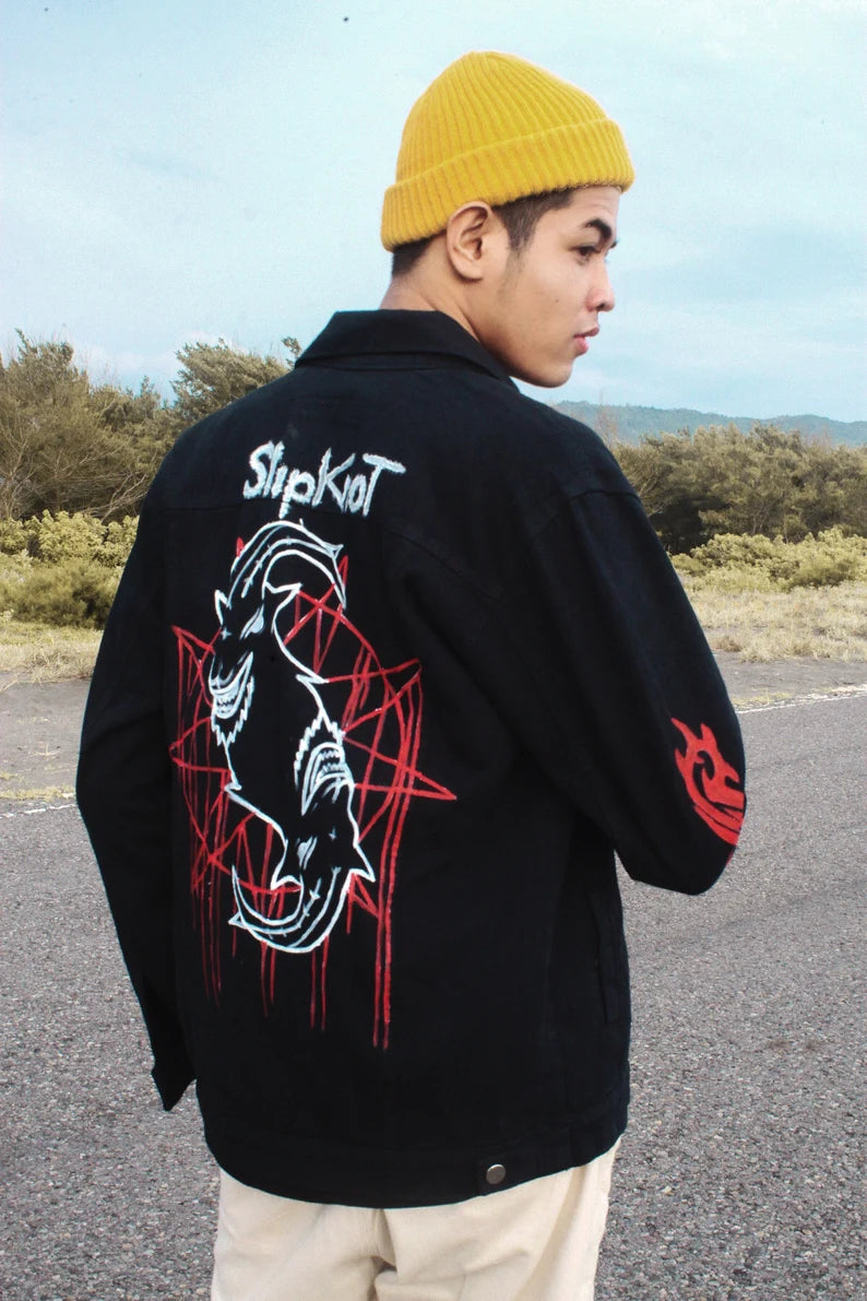 Person wearing a Bespoke Heavy Metal Clothing black jacket with red and white graphics and 'Slipknot' branding outdoors.