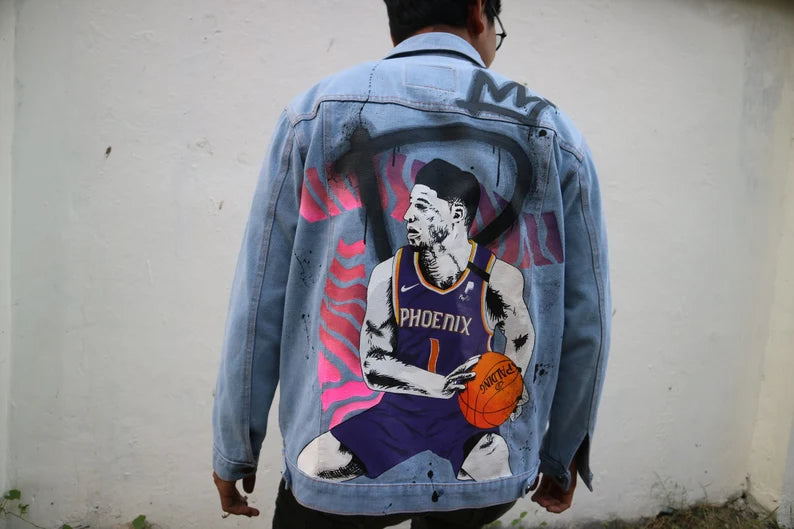 Multi-layered Hand-Painting Basketball Heritage denim jacket with a basketball player graphic on the back against a white wall.