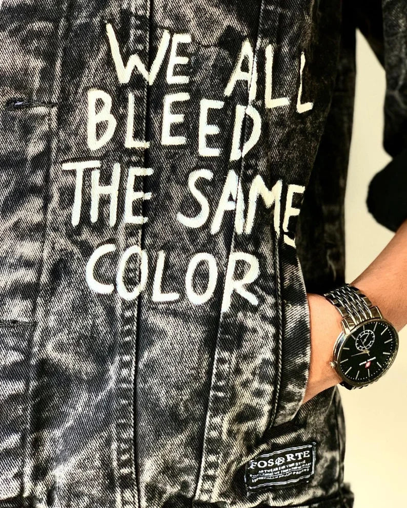 Human Rights Social Justice Denim jacket with text 'WE ALL BLEED THE SAME COLOR' and a watch on a neutral background