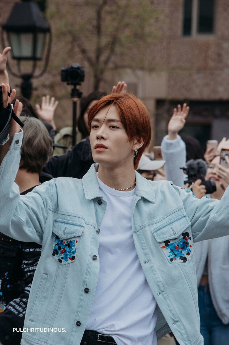 Person with red hair wearing a light blue Korean Style Denim Jacket with floral patches, surrounded by people outdoors.