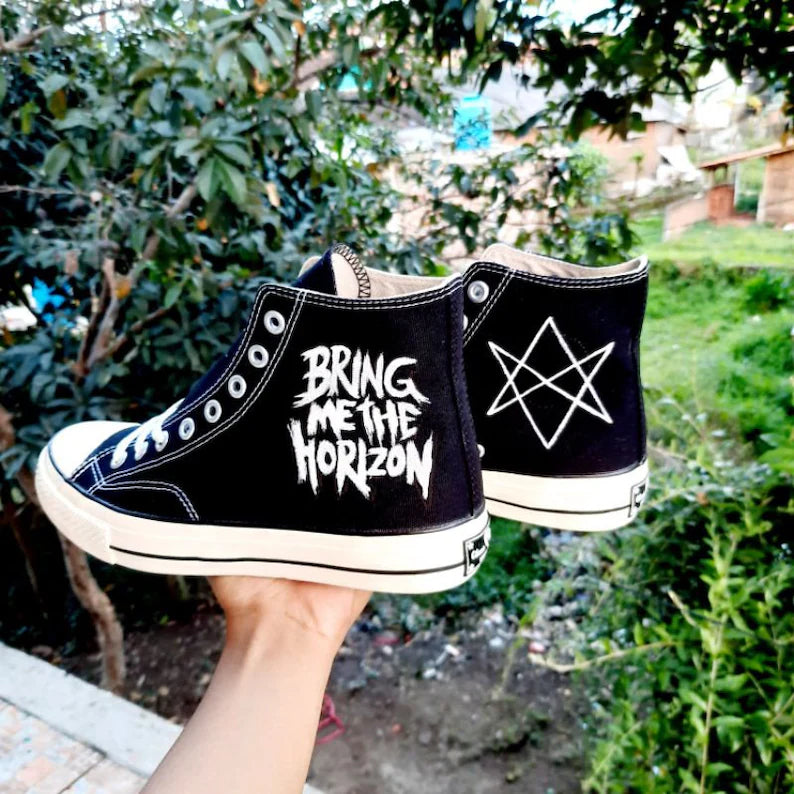 glow in the dark Black high-top sneakers with 'Bring Me the Horizon' logo held in front of green foliage.