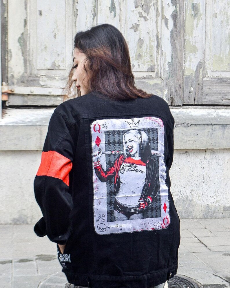 Person wearing a Harley Quinn jacket with a graphic design on the back, standing in front of a textured wall.