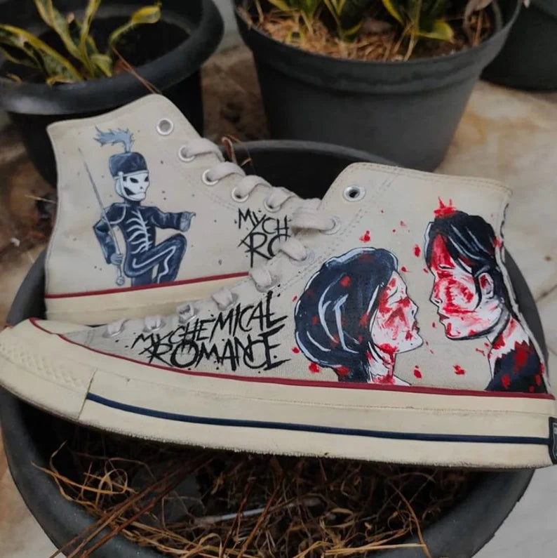 MCR Merch Hand-painted sneakers with artistic designs and text, placed on a surface with plants in the background.