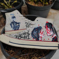 MCR Merch Hand-painted sneakers with artistic designs and text, placed on a surface with plants in the background.