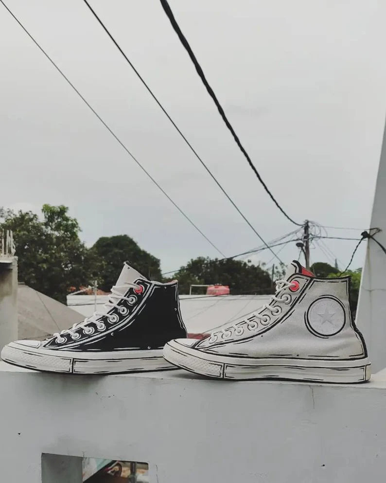 Black and white high-top sneakers with red accents on a ledge with power lines and trees in the background.