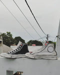 Black and white high-top sneakers with red accents on a ledge with power lines and trees in the background.