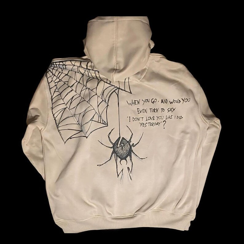 Beige hoodie with spider and web design on a black background punk rock concert outfit