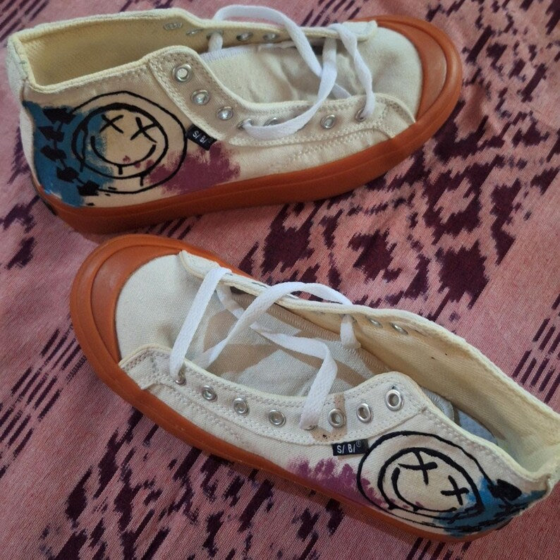 Skater Outfit Ideas Blink 182 Pair of beige sneakers with black smiley face design on a pink patterned surface