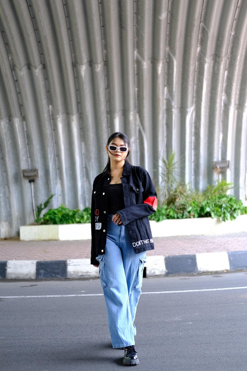 Person wearing a Graffiti black jacket with red accents and light blue jeans standing on a street.