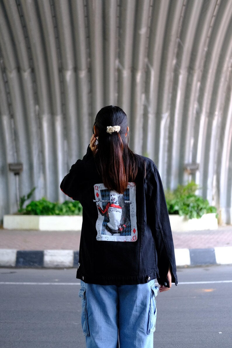 Person wearing a Harley Quinn Costume jacket with a graphic design on the back, standing in an urban setting.