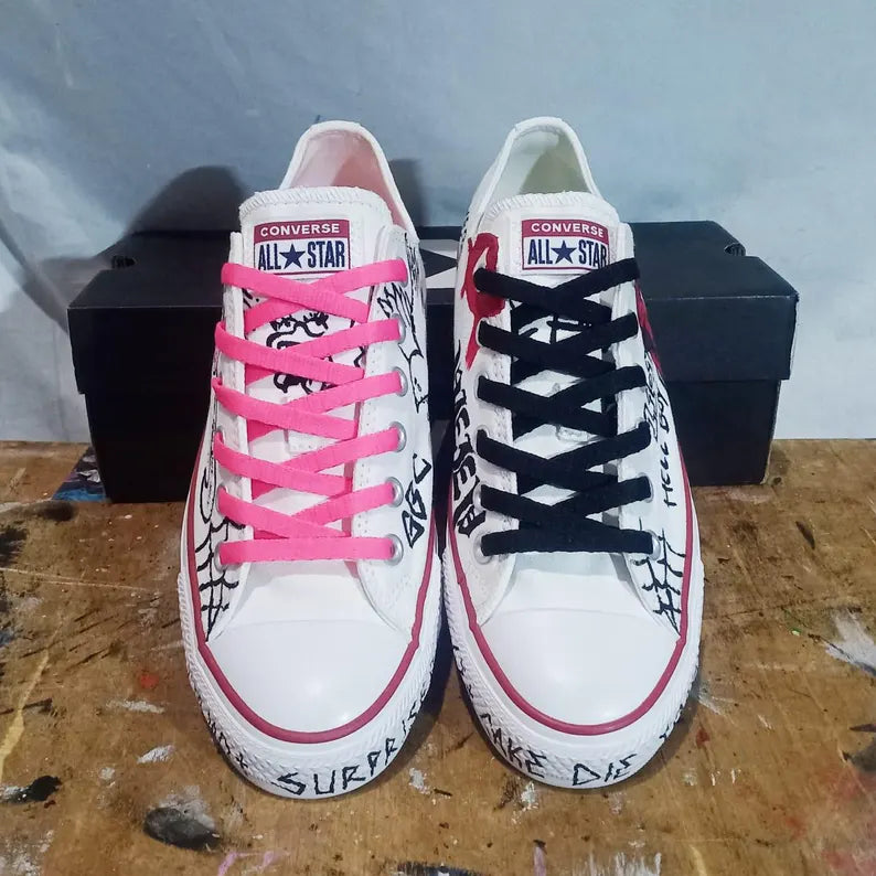 Pair of white Converse All Star lil peep sneakers with colorful laces on a wooden surface.