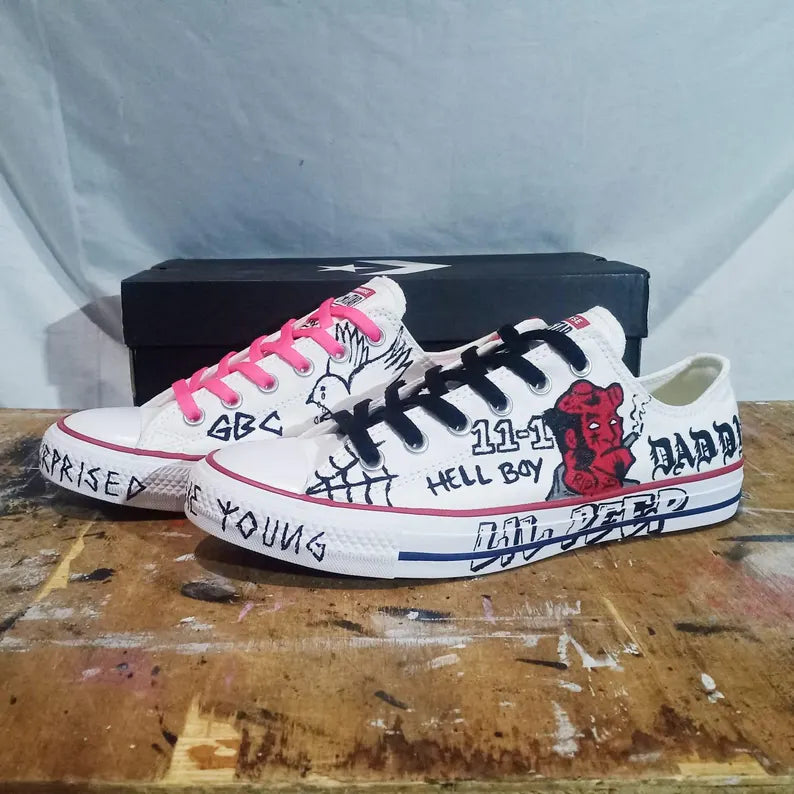 Goth Boi Clique Merch White sneakers with black text and graphics on a wooden surface