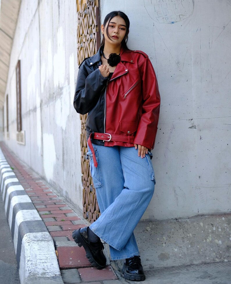 Person wearing a Street Art red and black leather jacket with blue jeans leaning against a wall.