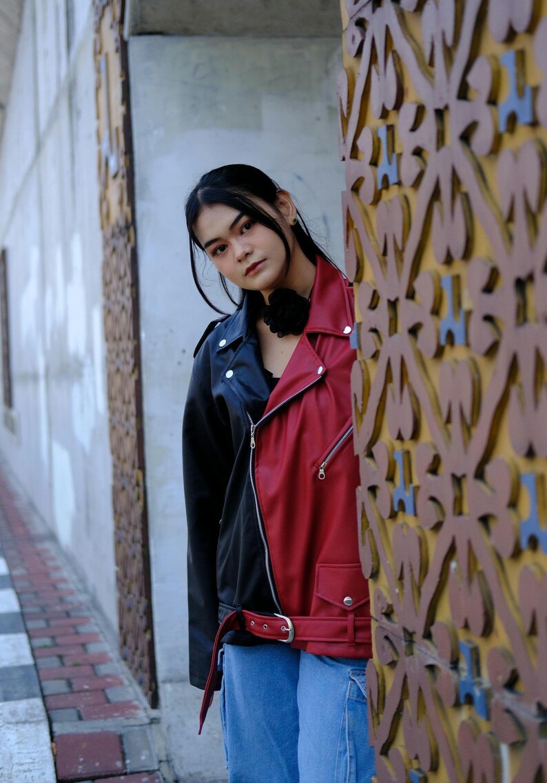 Person wearing a Abstract Grunge black and red jacket standing next to a textured wall.